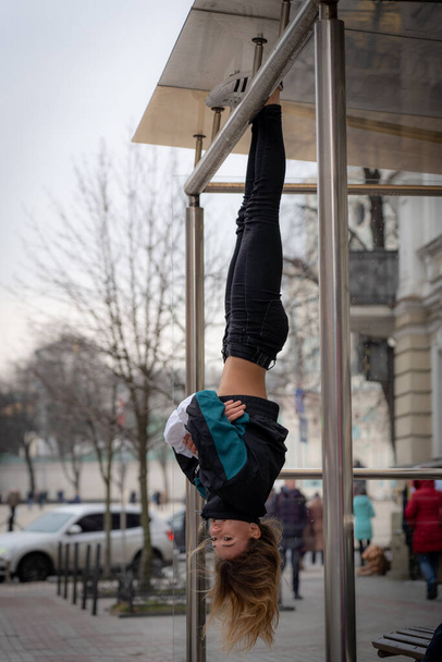 Young attractive Girl hanging by feet upside down in the street  - Fotoğraf, Görsel
