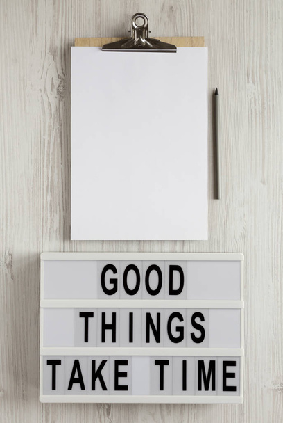 'Good things take time' words on a modern board, clipboard with blank sheet of paper on a white wooden background, top view. Overhead, from above, flat lay. - 写真・画像