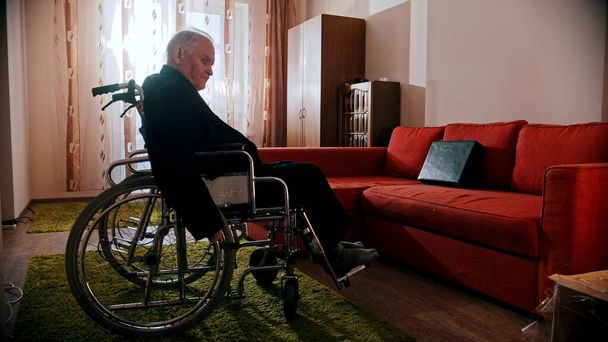 Um velho sentado em uma cadeira de rodas na sala
 - Foto, Imagem