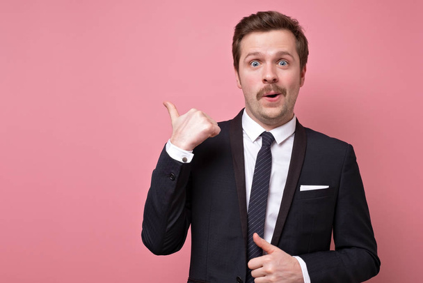 Mid adult serious business man with retro mustache and suit pointing to copy space isolated on pink background. Pay attention to this information. - Valokuva, kuva