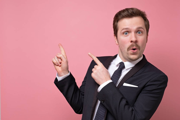 Mid adult serious business man with retro mustache and suit pointing to copy space isolated on pink background. Pay attention to this information. - Fotoğraf, Görsel