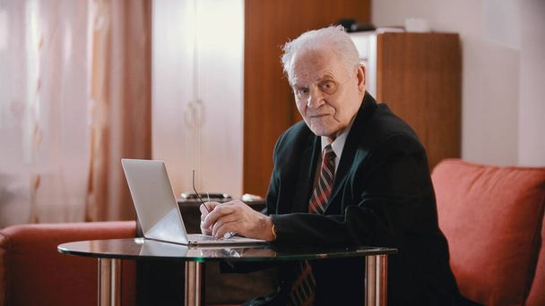 Un anciano sentado junto a la laptop y mirando a la cámara
 - Foto, imagen