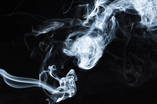 Background image of a wisp of smoke on a dark background. The texture of the flowing smoke. Frozen smoke on a dark background. Graphic resources dark backdrop. Texura of white clouds of fog. Curls of smoke frozen in motion. - Foto, Imagen