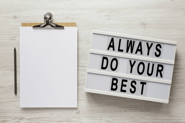 "Mach immer dein Bestes" steht auf einem modernen Brett, Klemmbrett mit leerem Blatt Papier auf einer weißen Holzoberfläche, Draufsicht. Über Kopf, von oben, flach gelegt.  - Foto, Bild