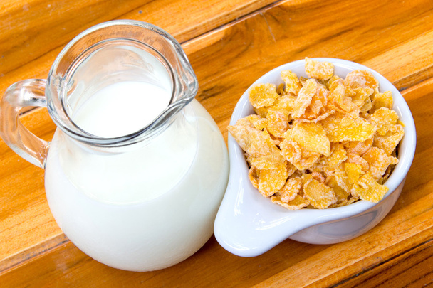 Maissihiutaleet valkoisessa kulhossa ja maito puupöydällä
 - Valokuva, kuva