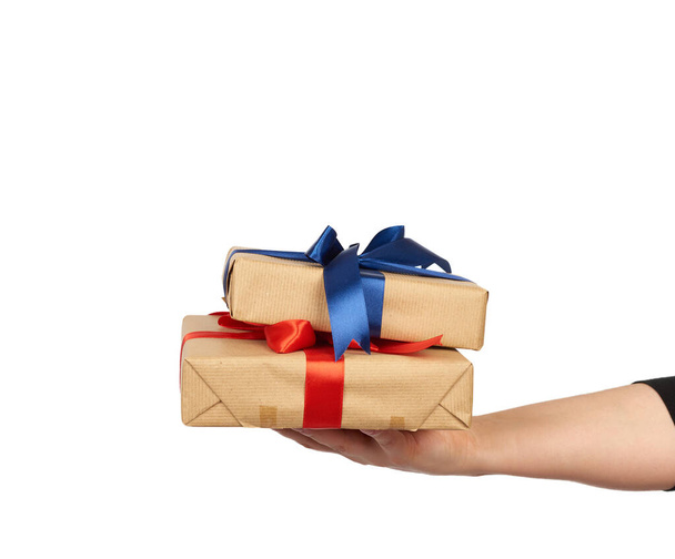 hand holds a stack of wrapped gifts in brown craft paper with tied silk bows, subject is isolated on a white background - Photo, Image