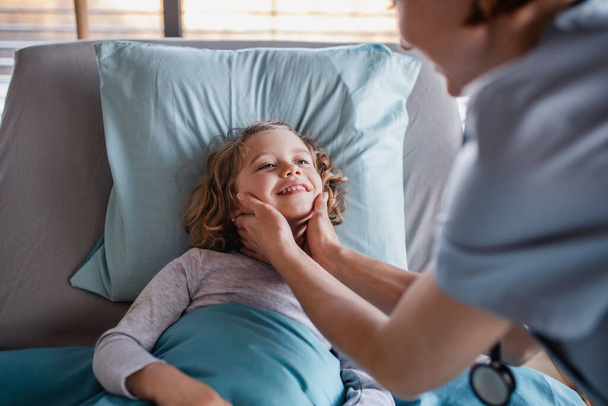 Friendly female doctor examining small girl in bed in hospital. - Valokuva, kuva