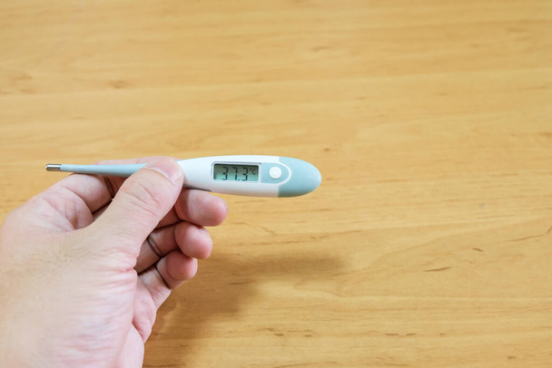 Los hombres sostienen el termómetro digital para medir la temperatura corporal y comprobar si hay fiebre en el fondo de madera. Enfermedad, asistencia sanitaria y concepto médico
. - Foto, Imagen