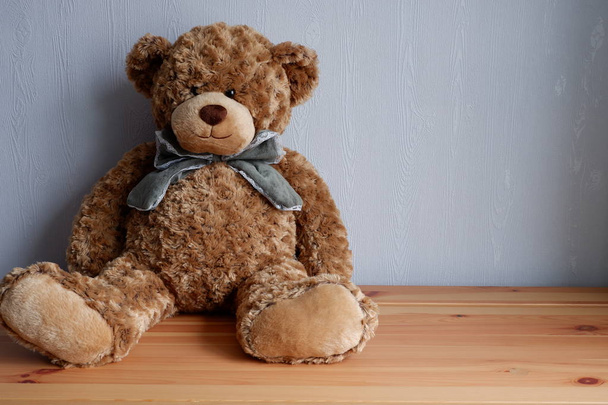Soft toy bear with a bow sitting on a wooden table - Фото, изображение