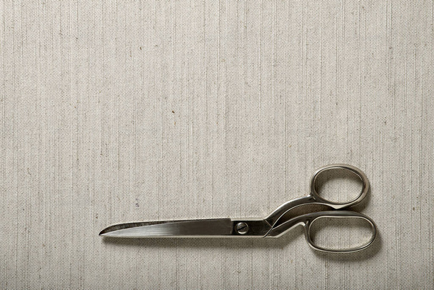 Beige rustic fabric background with scissors at its base - Valokuva, kuva