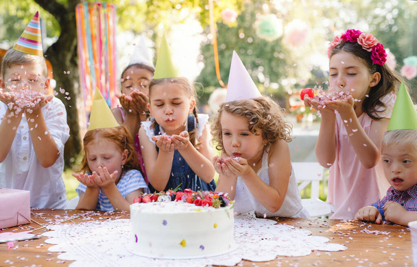 Children with cake standing around table on birthday party in garden in summer. - Photo, Image