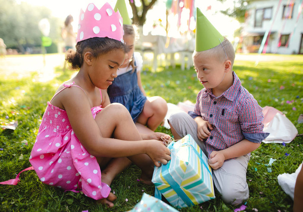 Down syndrome child with friends on birthday party outdoors, opening presents. - Foto, Imagem
