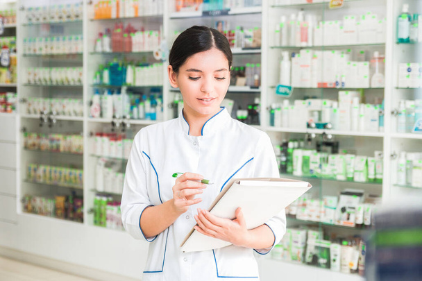 smart and confident woman pharmacist holding a folder and making notes - Photo, Image