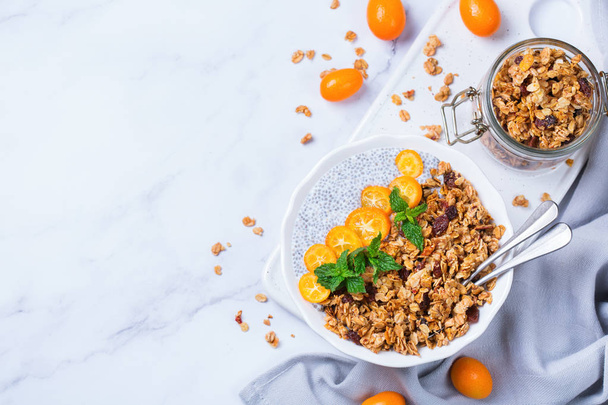 Organic vegetarian healthy eating and dieting food concept. Vegan chia pudding bowl with fresh homemade granola, orange kumquat and green mint for breakfast. Top view flat lay - Zdjęcie, obraz