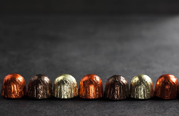 Line of chocolate candies wrapped in multicolored foil on black background with copy space - Photo, Image