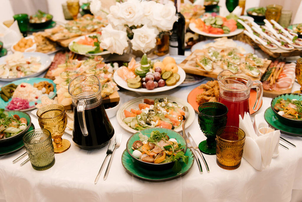 Круглый белый стол наполнен большим количеством еды и различных закусок в роскошном интерьере, красивая подача праздничного стола - Фото, изображение