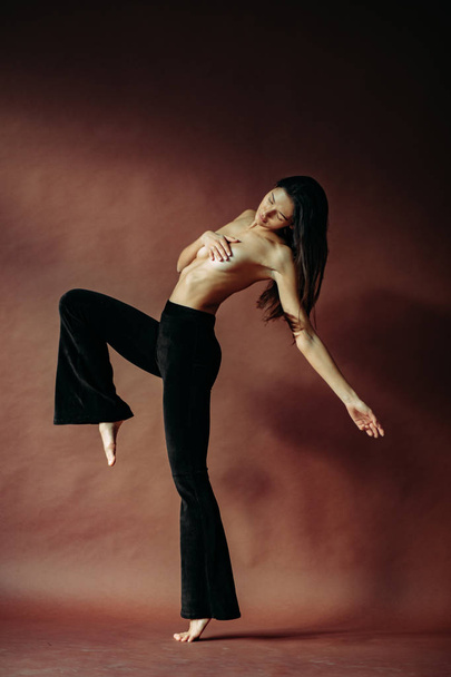 Junge Oben-Ohne-Frau tanzt in Hose im Studio. - Foto, Bild
