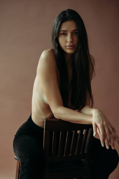 Young topless woman posing in the studio sitting on chair. - Фото, зображення