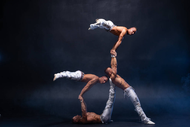 Four muscular man perform difficult acrobatic tricks on black studio  - Фото, зображення