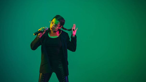 Caucasian female singer portrait isolated on green studio background in neon light - Zdjęcie, obraz