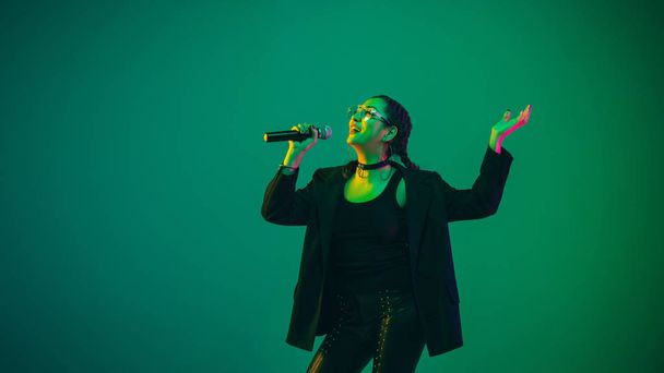 Caucasian female singer portrait isolated on green studio background in neon light - Foto, imagen