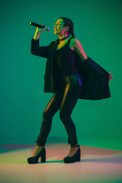 Caucasian female singer portrait isolated on green studio background in neon light - Fotografie, Obrázek