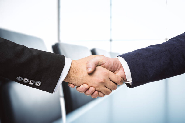Two businessmen shake hands on the background of sunny meeting room, deal concept, close up - Valokuva, kuva