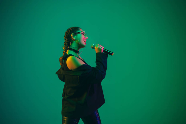 Caucasian female singer portrait isolated on green studio background in neon light - Fotoğraf, Görsel