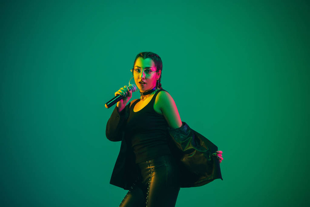 Caucasian female singer portrait isolated on green studio background in neon light - Foto, Imagem