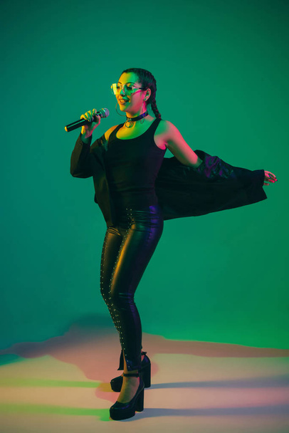 Caucasian female singer portrait isolated on green studio background in neon light - Foto, Imagem