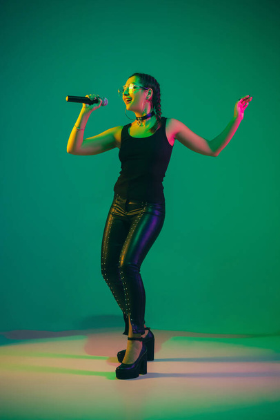Caucasian female singer portrait isolated on green studio background in neon light - 写真・画像
