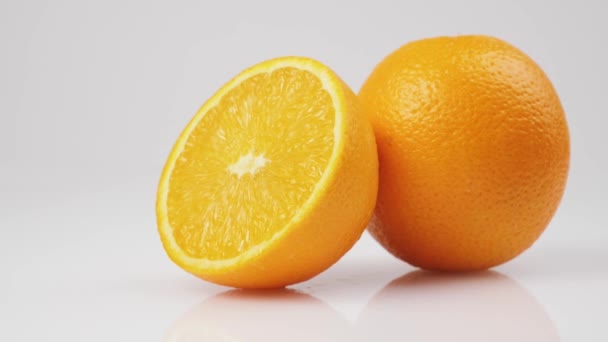 Midden schot van twee verse sinaasappels draaien om zijn as op een witte tafel tegen een witte achtergrond, geïsoleerd - Video