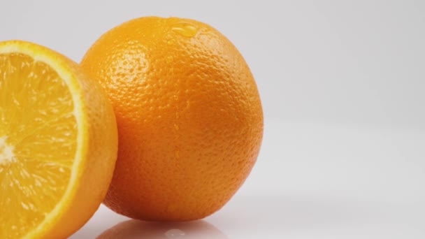 白い背景を背景に白いテーブルの上に新鮮なオレンジをゆっくりと流れる水の滴の中のショット,隔離で - 映像、動画