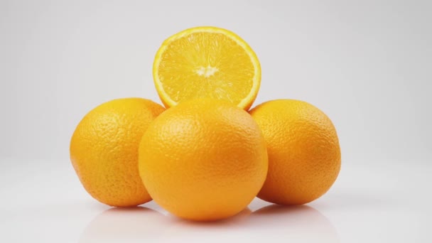 Μεσαίο πλάνο από δέσμη πορτοκαλιών περιστρέφεται στον άξονά του σε ένα λευκό τραπέζι σε λευκό φόντο, σε απομόνωση - Πλάνα, βίντεο