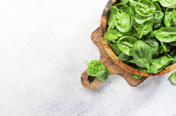 Fresh baby spinach leaves in wooden bowl on gray stone table. Top view, copy space - Фото, зображення