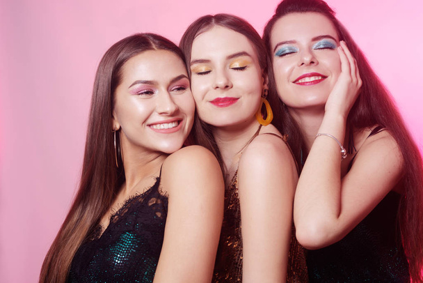 3 chic girls, portraits of models with chic bright makeup. Girls in shiny clothes, with accessories, earrings, bright makeup on a pink background. Holiday, party. March 8, Women's Day. - Photo, Image