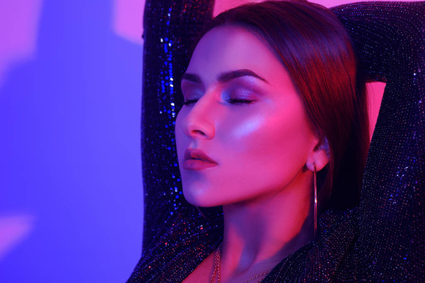 Portrait of a gorgeous brunette with big lips, perfect eyebrows, in big earrings, ringlets. A chic girl in a nightly dance, dancing to songs, in a neon light. A party. - Foto, imagen