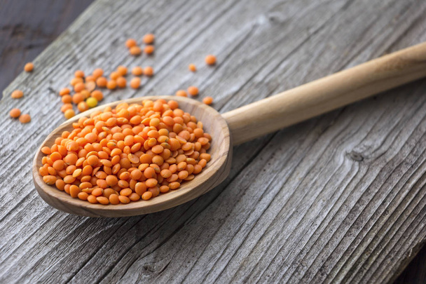 Red lentils on wooden spoon at plank background.  - Photo, Image
