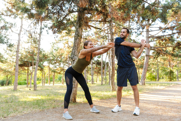 Photo of attractive cheerful couple in sportswear doing exercises while working out in green park during sunny summer day - Valokuva, kuva