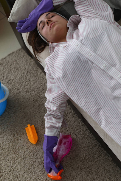 Menina em luvas para limpeza encontra-se sofá de fadiga
 - Foto, Imagem