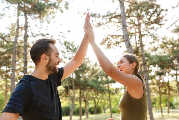 Image of a young positive sports woman and man outdoors in nature green park give a high-five to each other. - Photo, Image