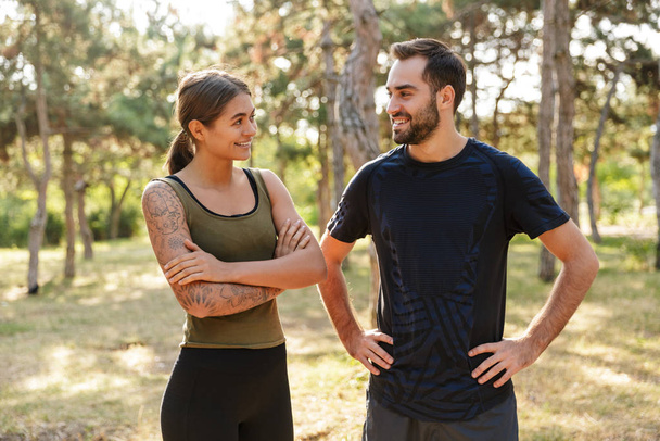 Image of a young strong positive sports woman and man posing outdoors in nature green park looking to each other. - Photo, Image