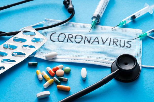 Beschermende gezichtsmasker, pillen, spuiten en stethoscoop op blauwe achtergrond, tegen Novel coronavirus 2019-ncov of Wuhan coronavirus. Hygiëne en gezondheidszorg concept - Foto, afbeelding