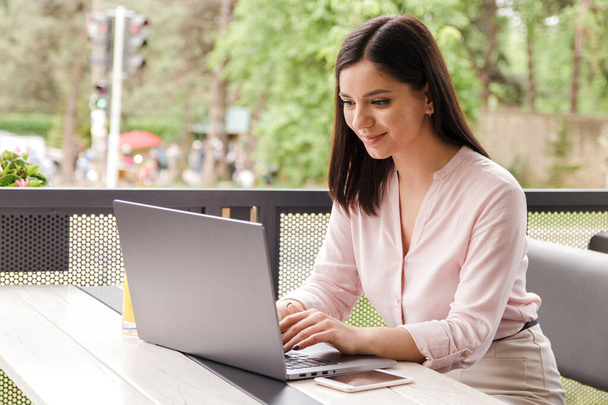 cheerful young businesswoman smiling working with energy on computer on terrace in cafe - Photo, Image