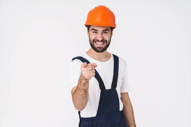 Photo of a pleased happy young man builder in helmet posing isolated over white wall background pointing to you. - Φωτογραφία, εικόνα