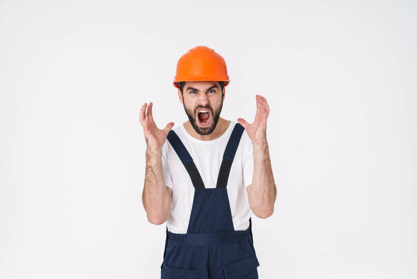 Photo of emotional screaming stressful young man builder in helmet posing isolated over white wall background. - Φωτογραφία, εικόνα