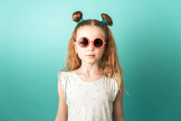 Bright colors: a girl in sunglasses on a green background. Studio portrait. - Foto, afbeelding