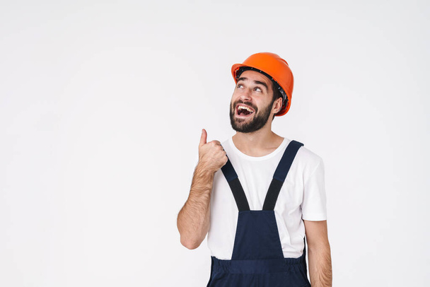 Photo of cheery happy young man builder in helmet posing isolated over white wall background pointing aside. - Foto, Imagen