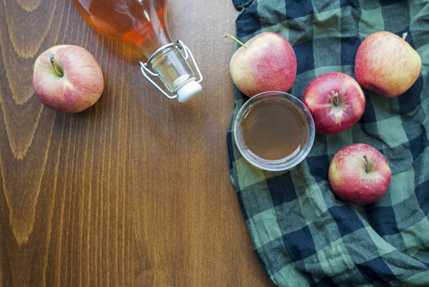 Top view of a bottle and glass.   Homemade apple juice. On a wooden table with a black-green checkered tablecloth. - Photo, Image