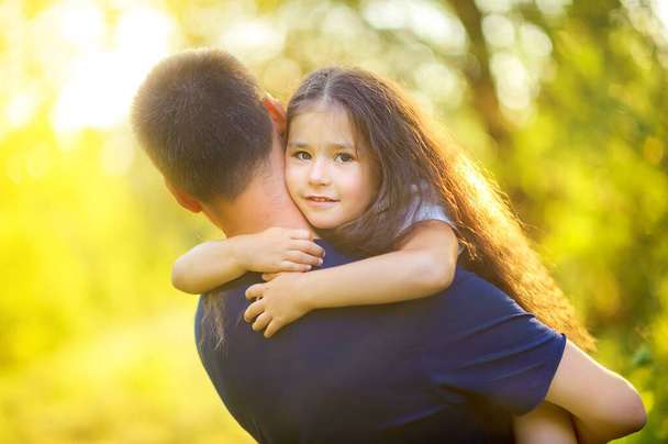 Happy family. Dad with his beloved daughter in his arms in the park at sunset, family time. - Foto, immagini